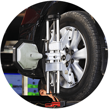 Circular image of a car on a lift with wheel alignment equipment attached to the front tire in an auto service shop.