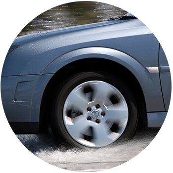 Circular photo of a silver car driving through shallow water, front wheel spinning and spraying small splashes