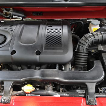 Top view of a clean modern car engine compartment with black plastic cover and visible hoses in a red vehicle.