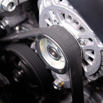Close-up view of a car engine’s serpentine belt wrapped around a shiny metal pulley and alternator components.