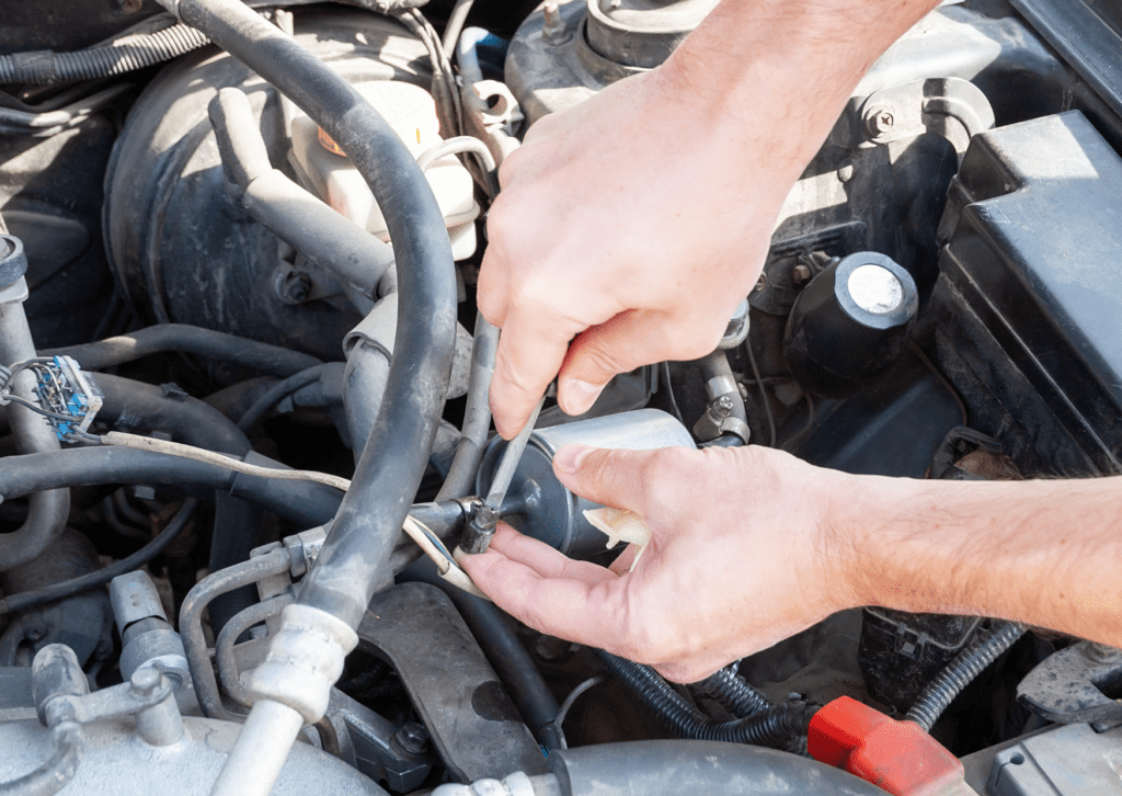 Close-up of hands using a screwdriver to repair a car's fuel system under the hood.