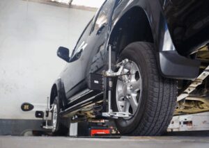 Black SUV undergoing 4 wheel alignment with sensors attached to each tire in an auto repair shop.