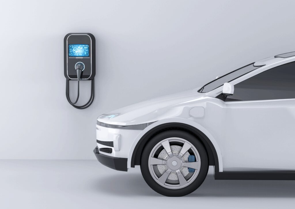 Side view of a white electric car parked indoors near a wall-mounted charging station, emphasizing modern EV technology.
