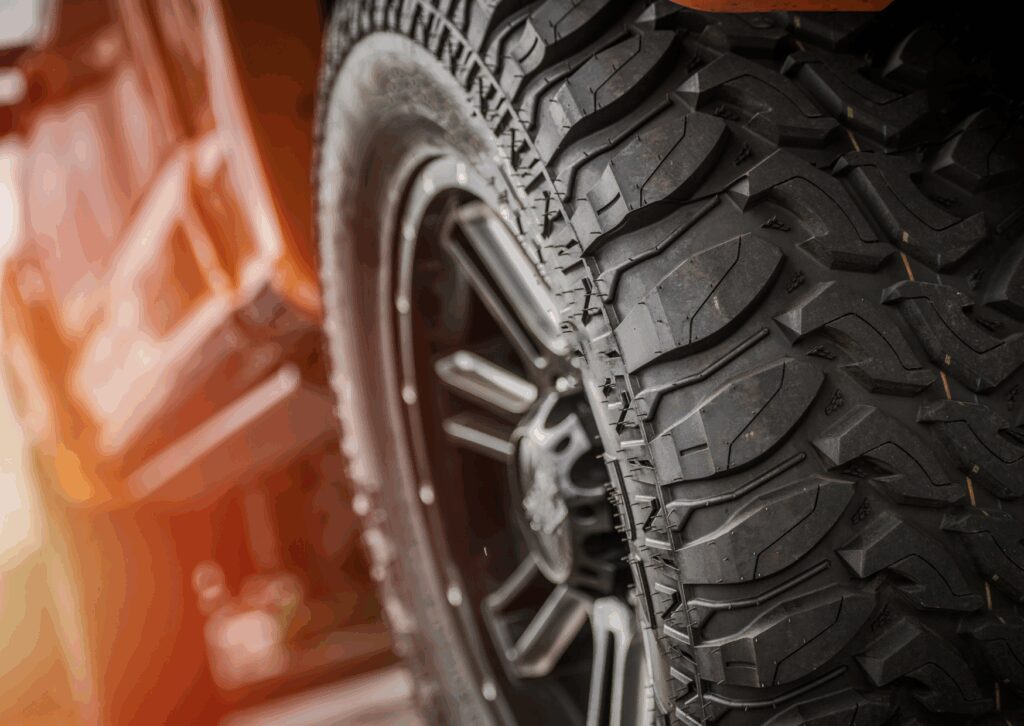 Close-up of rugged all-terrain tire on an off-road vehicle, showing tread pattern and sidewall detail in warm light.