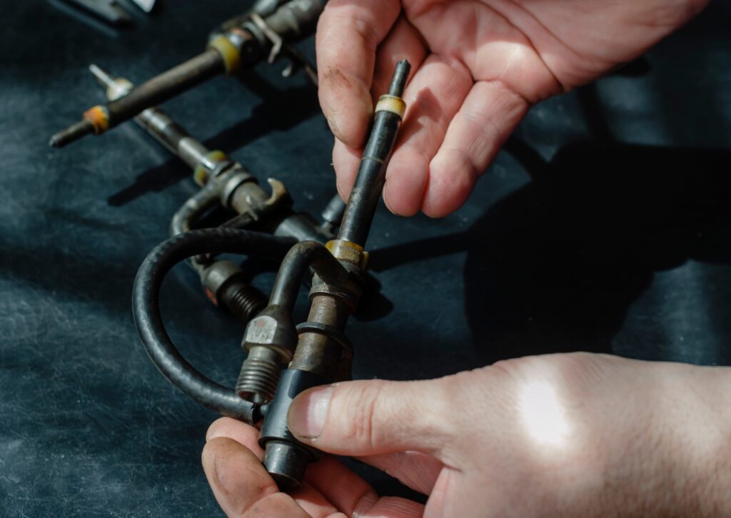 Hands inspect diesel fuel injector and lines on workbench, checking seals and fittings during engine repair work.