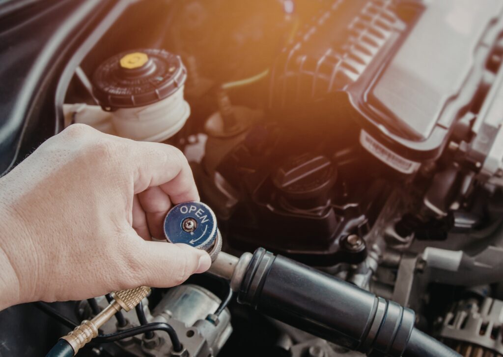 Hand opens a pressure gauge valve on engine bay, testing lines and components during automotive diagnostic service and repair.