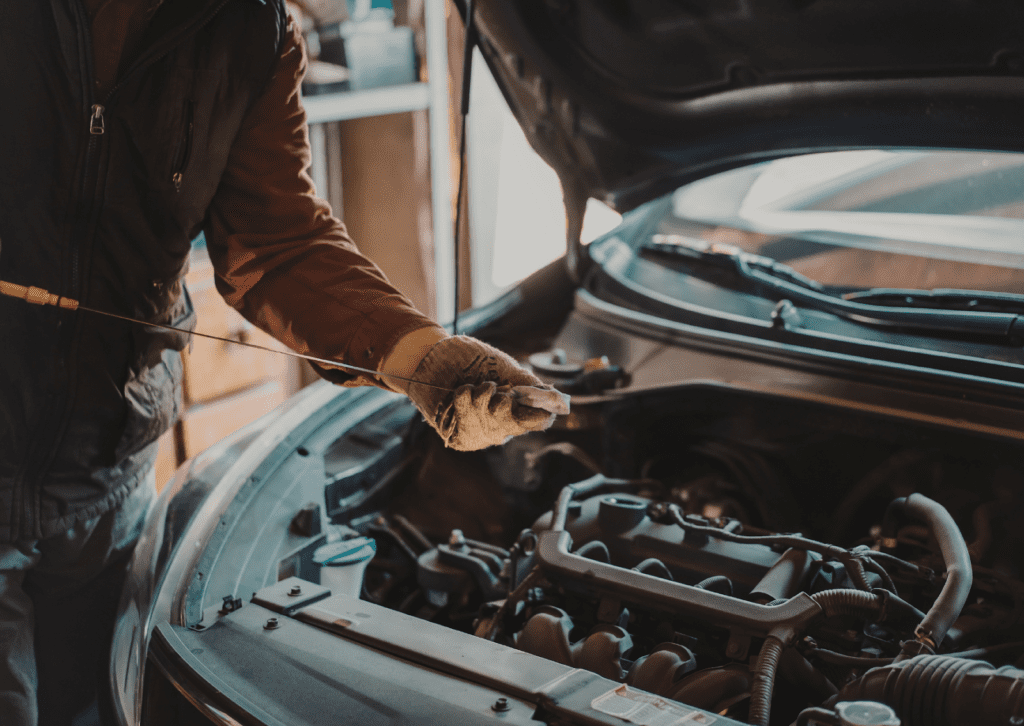 Fresh motor oil poured from black bottle into yellow funnel in car engine bay during oil change service.