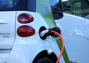 White electric car plugged into charging port with orange cable, rear view showing electric drive badge.