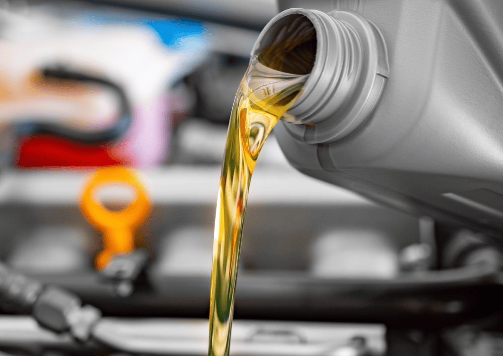 Golden motor oil pouring from a gray bottle into an engine bay during routine vehicle maintenance. 