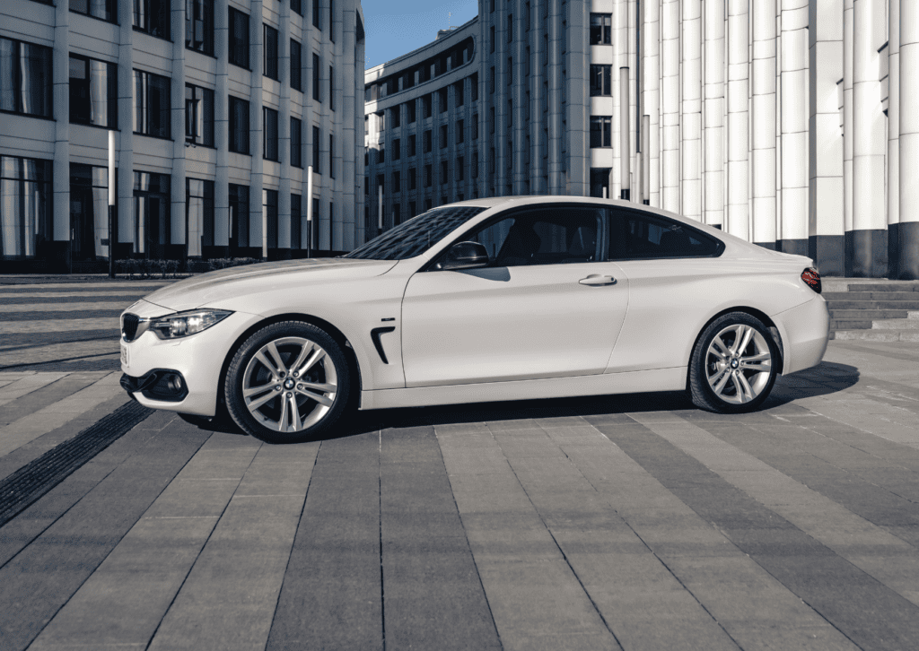 White BMW coupe parked in a modern plaza surrounded by tall contemporary office buildings. 