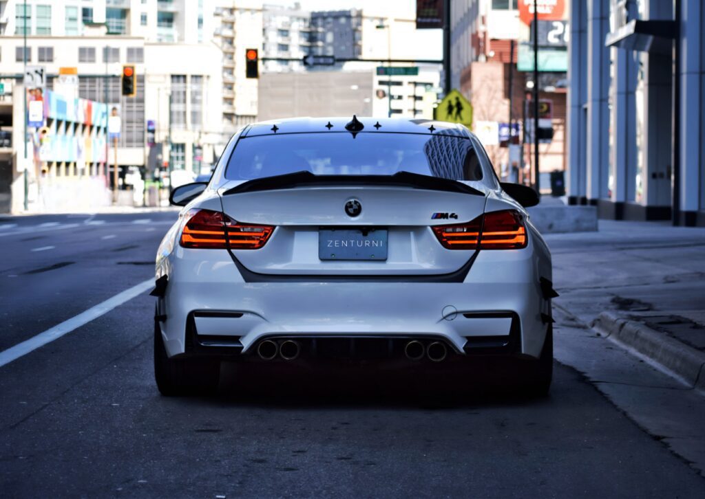 Rear view of a white BMW M4 parked on a city street, showing taillights and quad exhaust pipes 