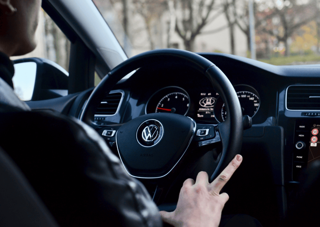 Driver behind the wheel of a Volkswagen vehicle, showing the steering wheel and dashboard controls 