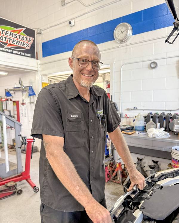 Metric Motors technician smiling next to a car with the hood up