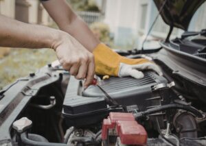 Mechanic uses screwdriver to check air filter housing under hood, illustrating signs your car needs a tune up.