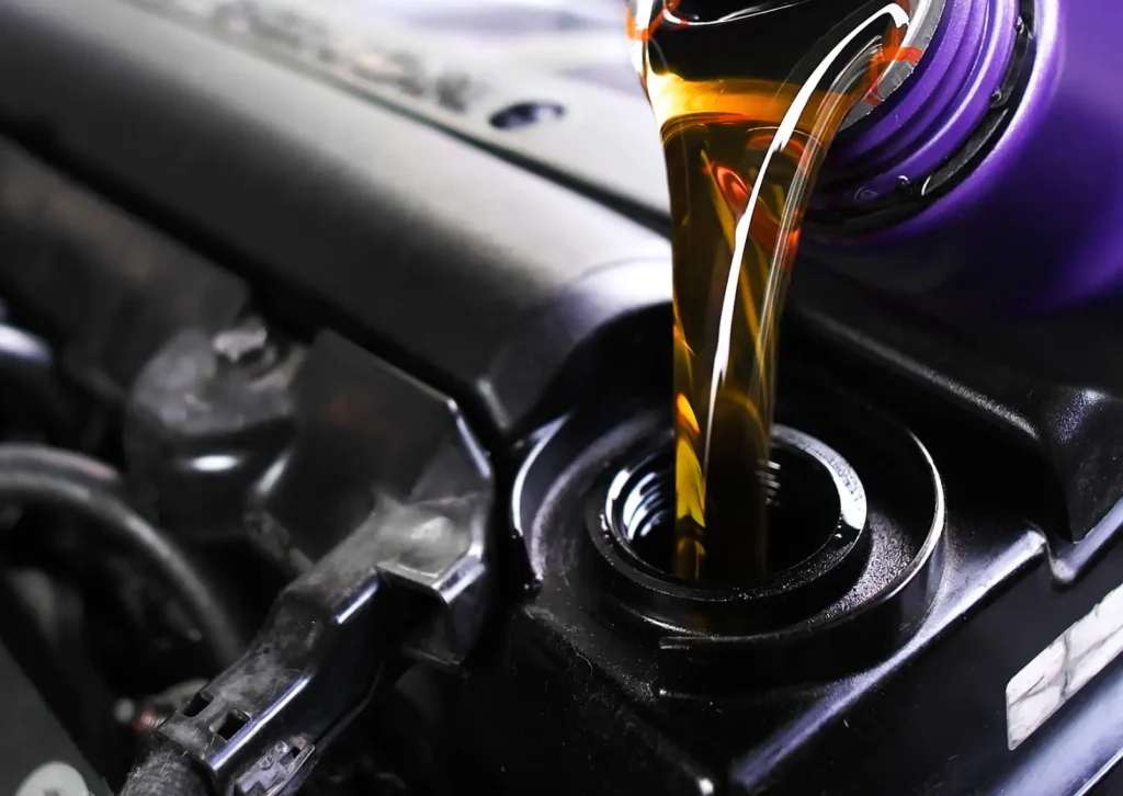 Close-up of fresh motor oil pouring from purple bottle into engine fill port during routine car service