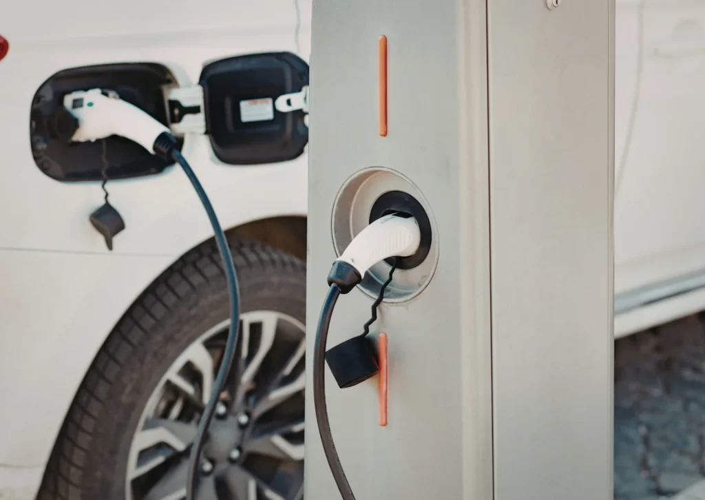 Electric car charging at public station, plug connected to vehicle port with cable beside rear wheel.