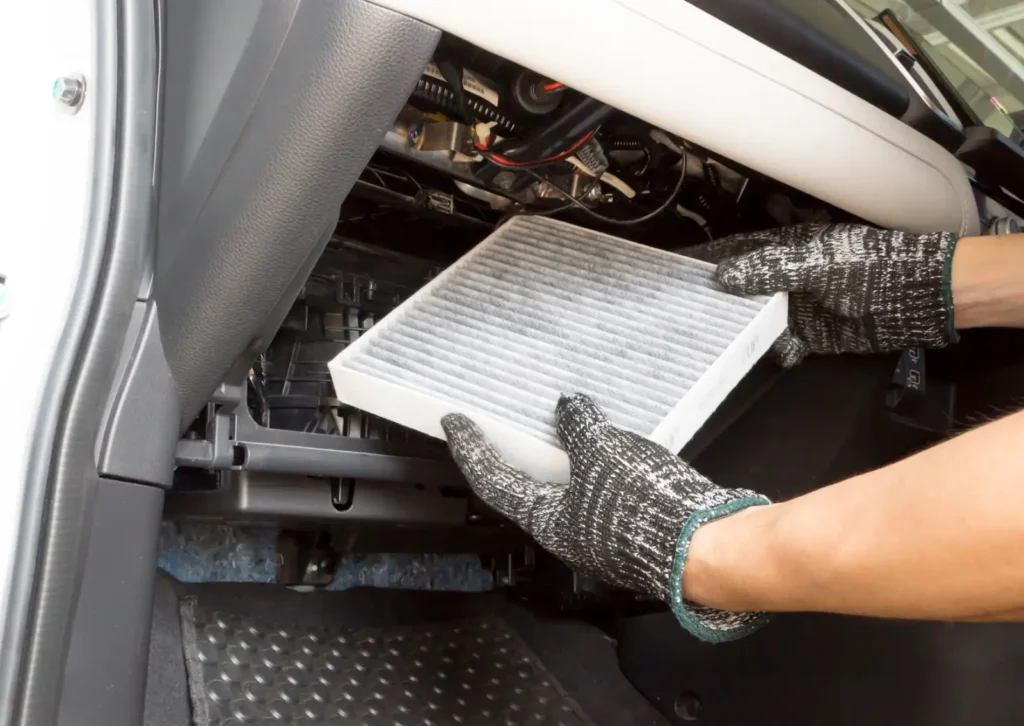 Gloved hands replace a cabin air filter inside the glove box compartment during routine car maintenance.