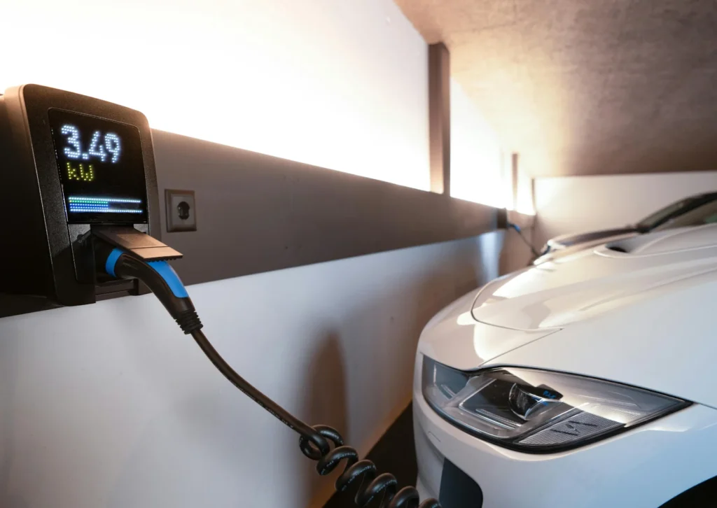 Wall-mounted EV charger display reads 3.49 kW as coiled cable charges a white car in a bright home garage.