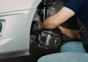 Mechanic repairs front brake and strut to diagnose car suspension noises during service check.