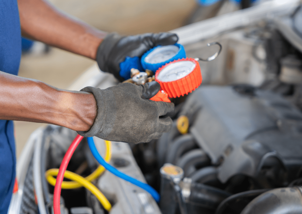 Technician holding AC pressure gauges while testing refrigerant levels inside vehicle engine bay 