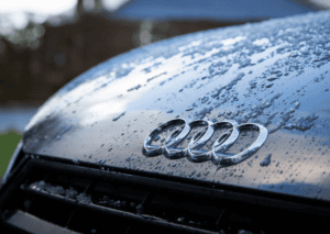Close-up of chrome Audi rings on a wet hood covered with water droplets and melting ice patches. 