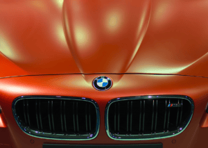 Close-up of a BMW emblem and twin kidney grille on a metallic orange car under showroom lights. 